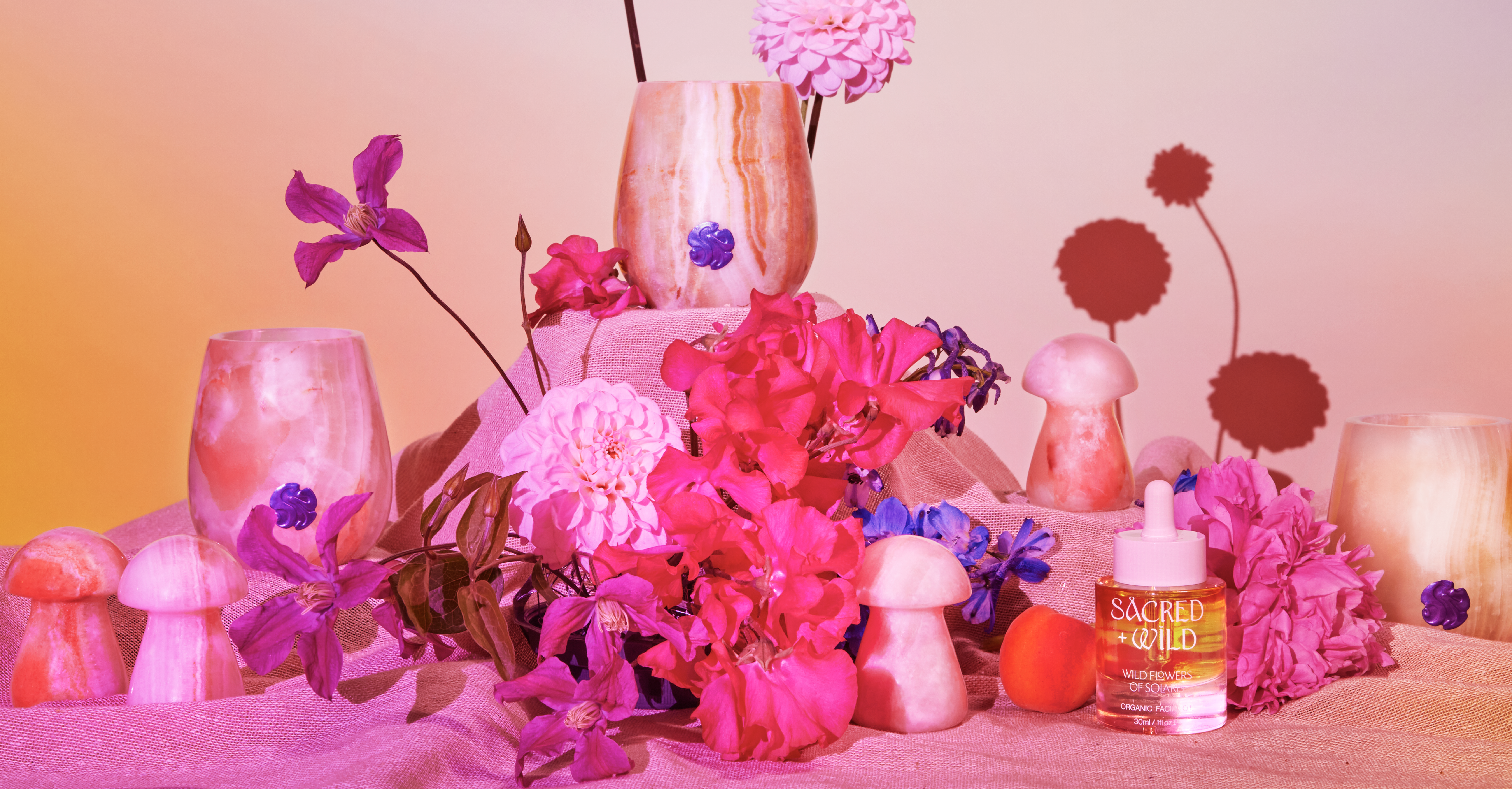 Selection of beauty products in a studio surrounded my flowers with pink colour effects